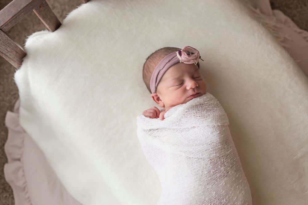 Sleeping newborn wrapped in white swaddle on plush cream surface.