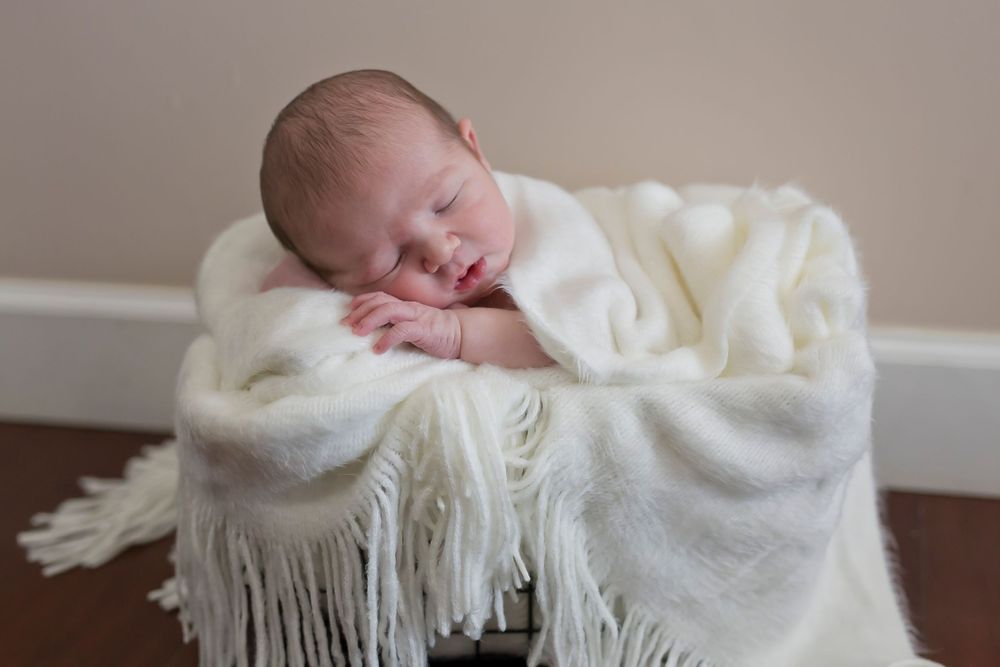 Sleeping baby wrapped in white textured blanket with fringe detail.