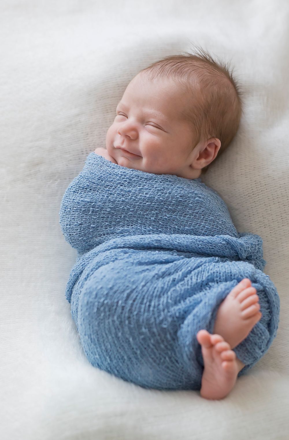 Sleeping newborn wrapped in light blue knit blanket showing tiny feet.