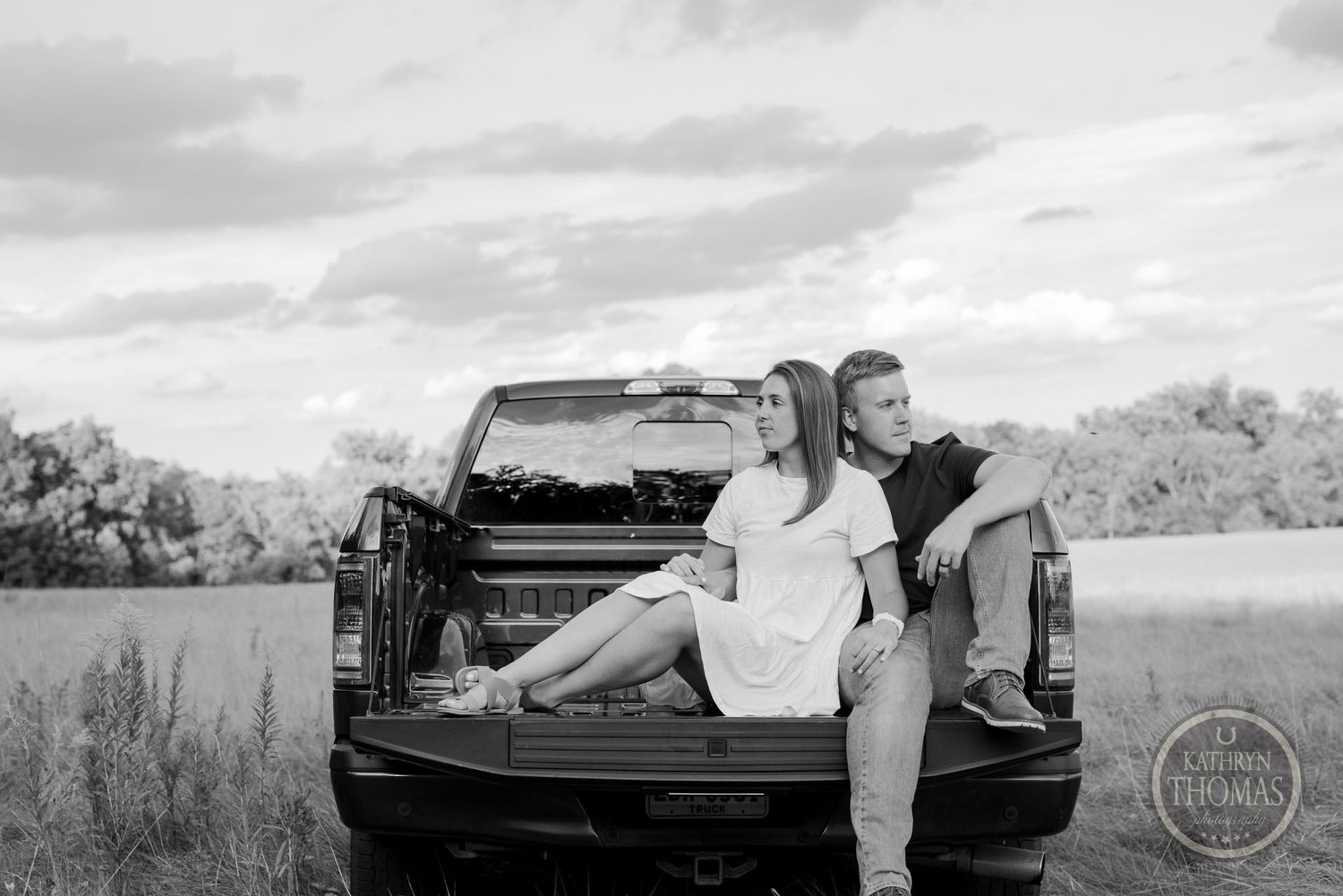 Black and white portrait of couple sitting in pickup truck bed outdoors.