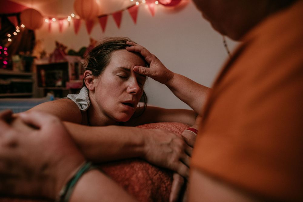 doula rubs birth persons forehead during water birth portland oregon birth photography