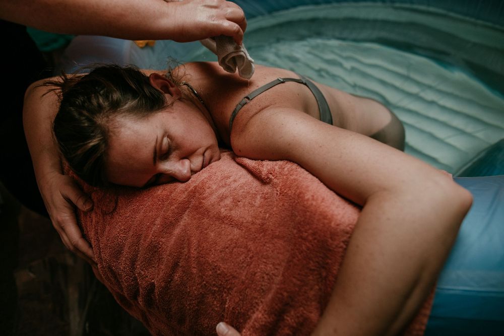doula uses wet washcloth on birth persons back during water birth portland oregon birth photographer