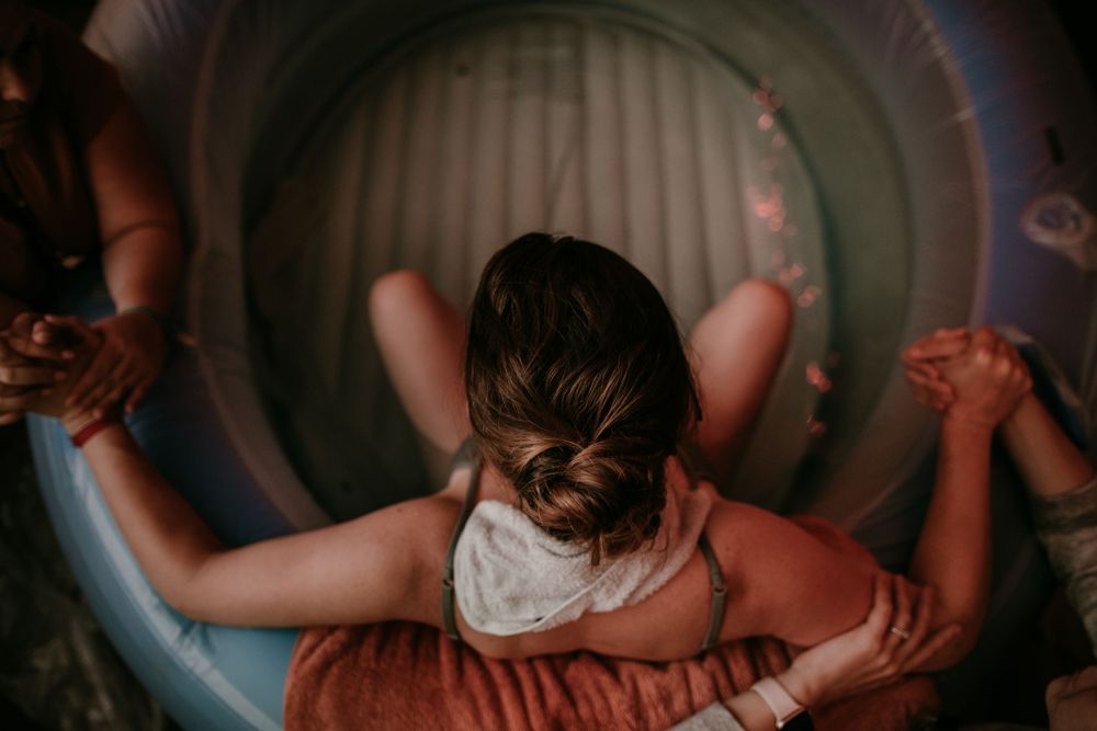 doula and midwife hold birthing persons hands during water birth portland oregon birth photographer