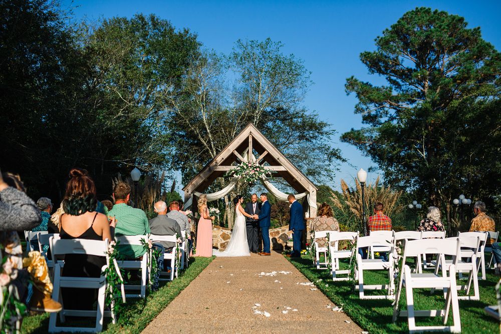 Wedding ceremony at rustic wooden gazebo with white chairs and natural surroundings.