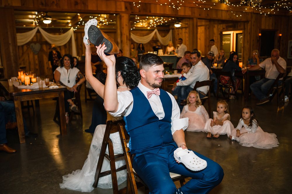 Playful wedding game moment during rustic barn reception with string lights.