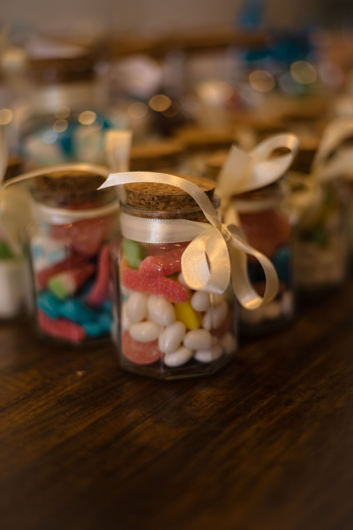 Small decorative candy jars lined up on wooden table with ribbons.