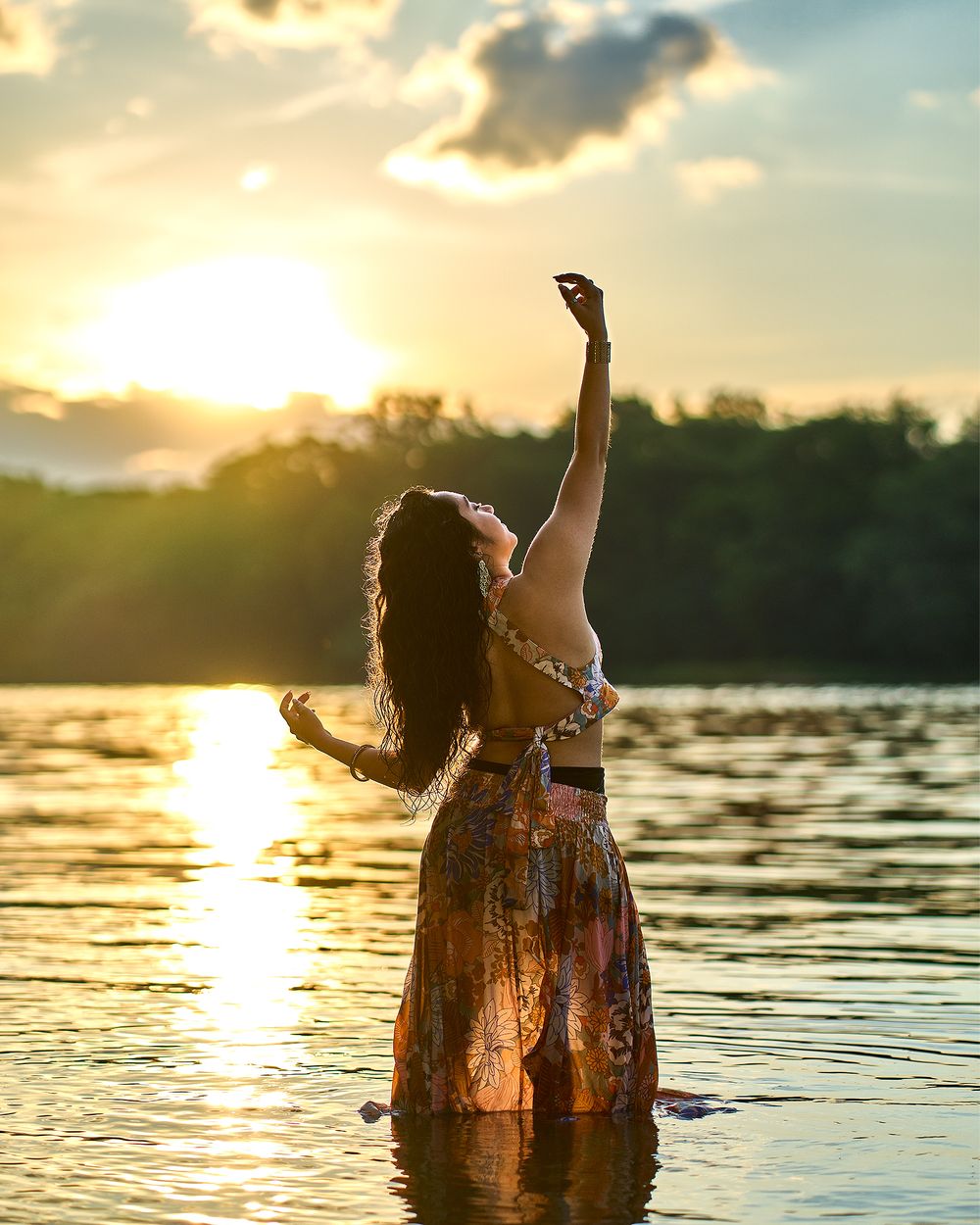 Silhouette of a person dancing in floral dress standing in water during golden sunset over a lake.