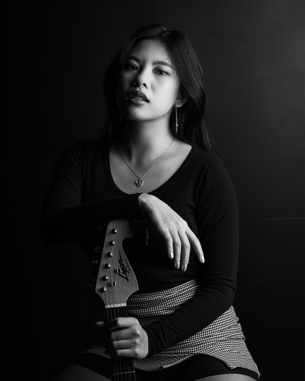 Dramatic black and white portrait with guitar headstock in foreground.