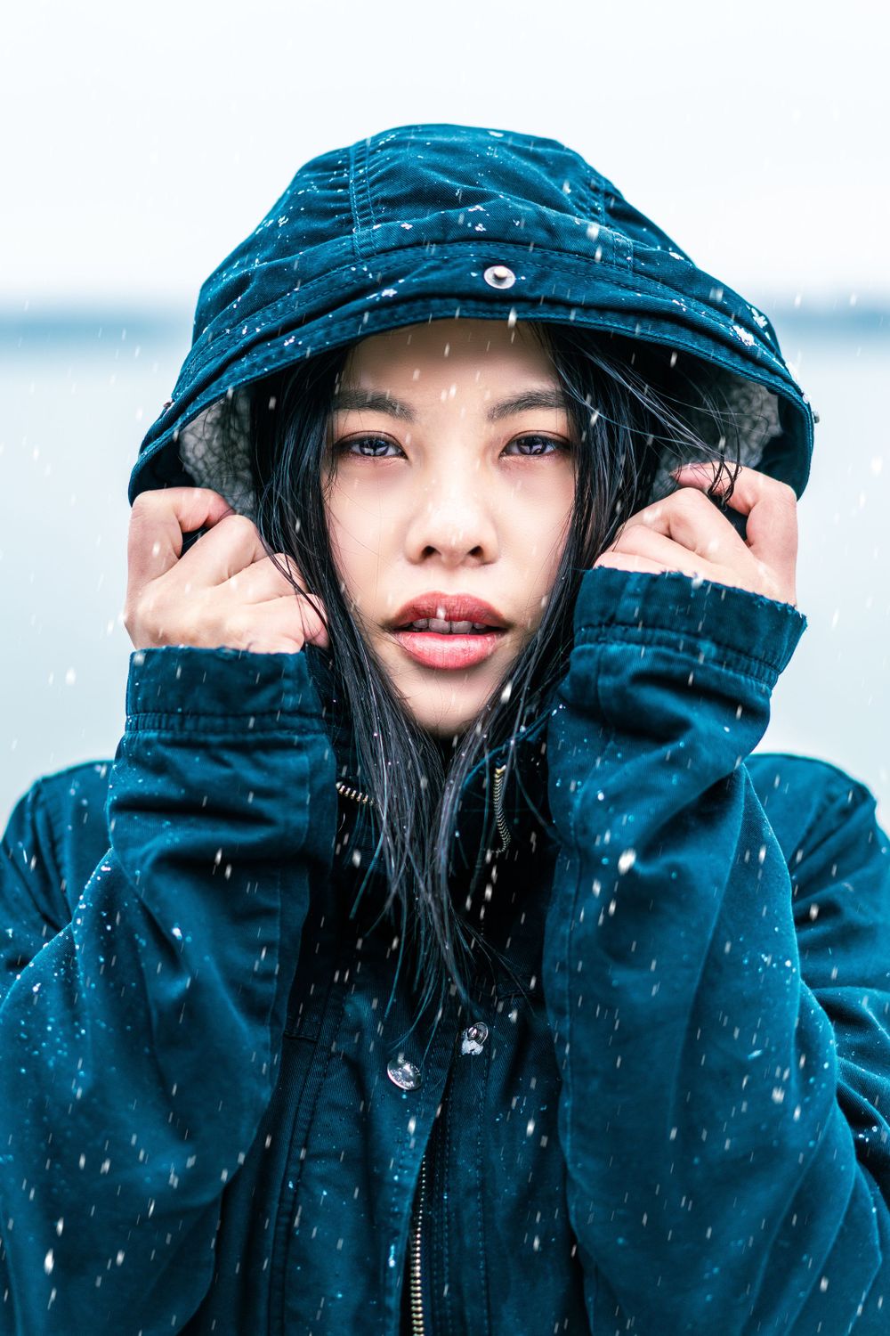 Person wearing blue winter coat and hood in snowy weather.