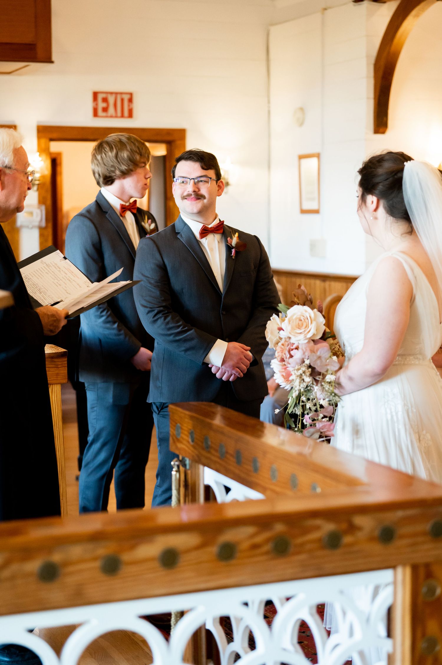 Wedding ceremony in progress with attendants gathered at the altar in a traditional chapel setting.