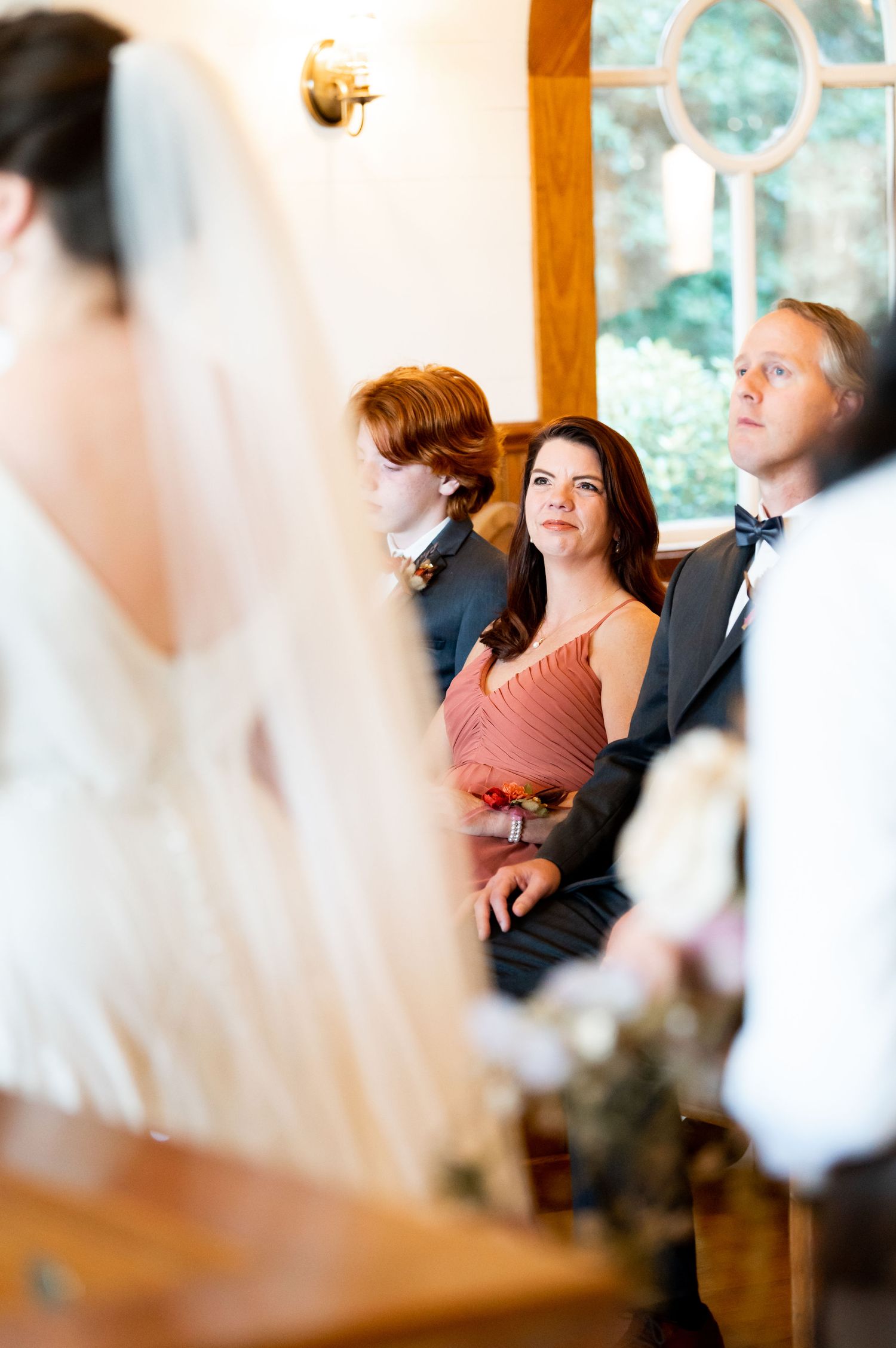 Wedding guests watching ceremony in a chapel with stained glass windows and wooden details.