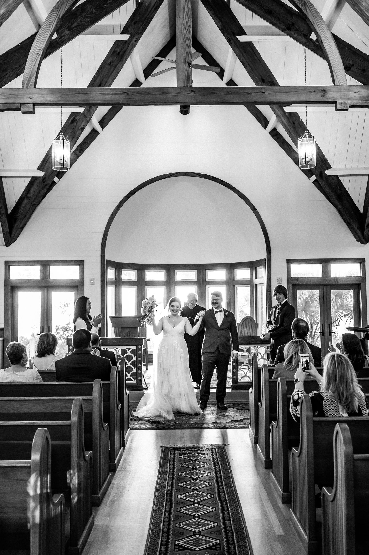 Wedding ceremony in a chapel with exposed wooden beams and guests seated in wooden pews.