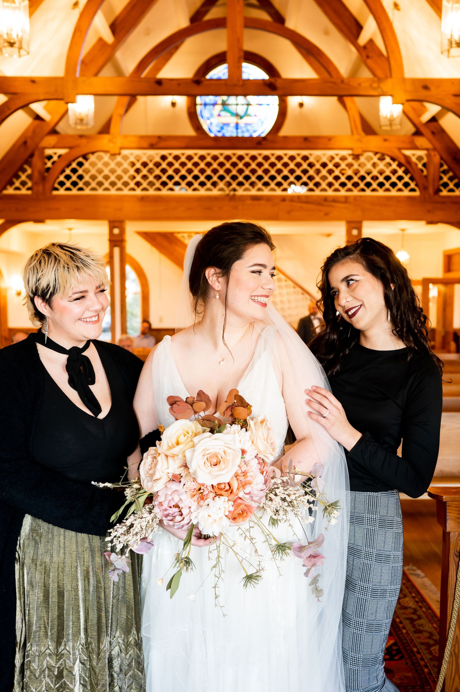 Three friends share a joyful moment in a chapel with warm lighting and wooden beams overhead.