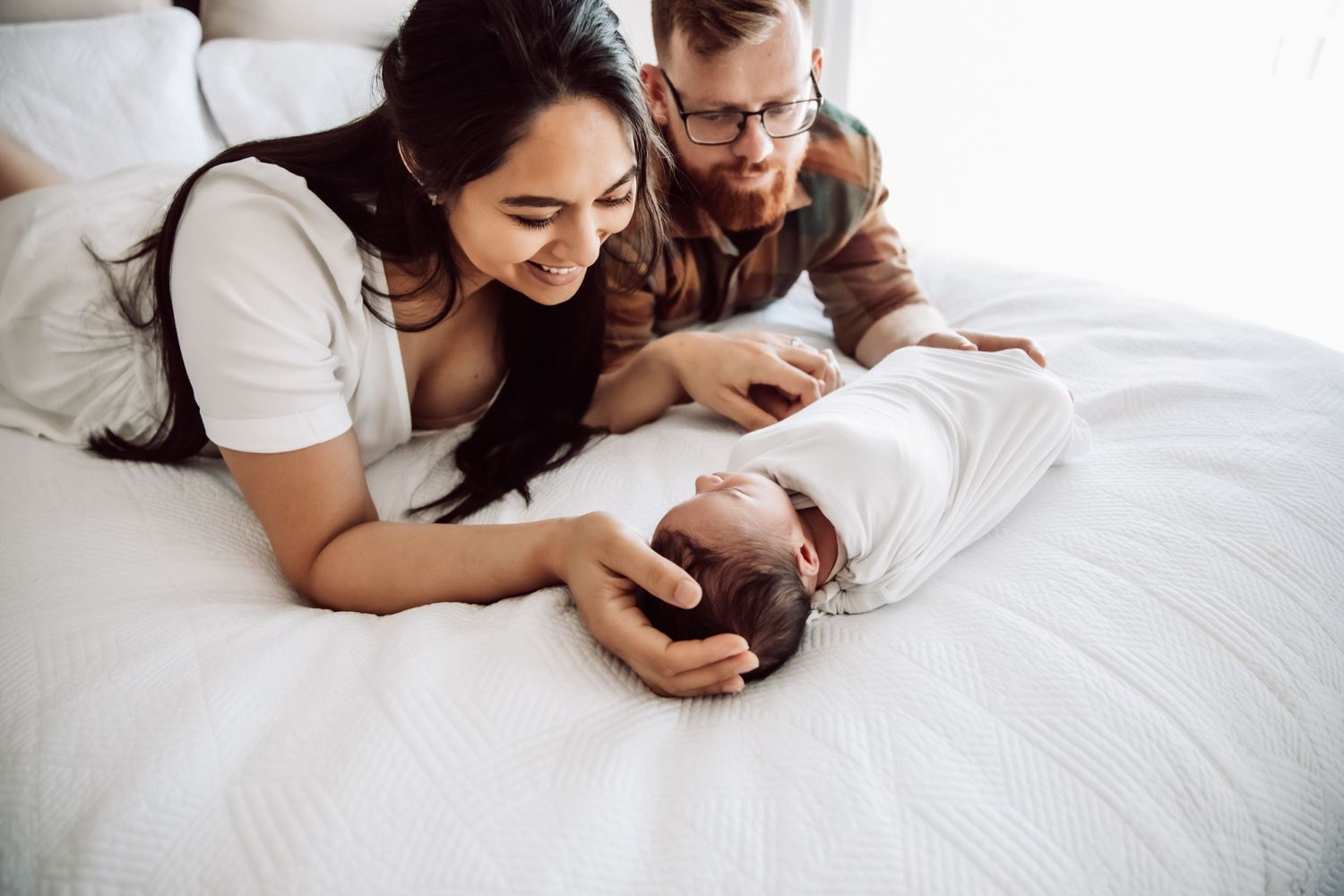 Close-up of parents gazing lovingly at their newborn baby on white bedding.
