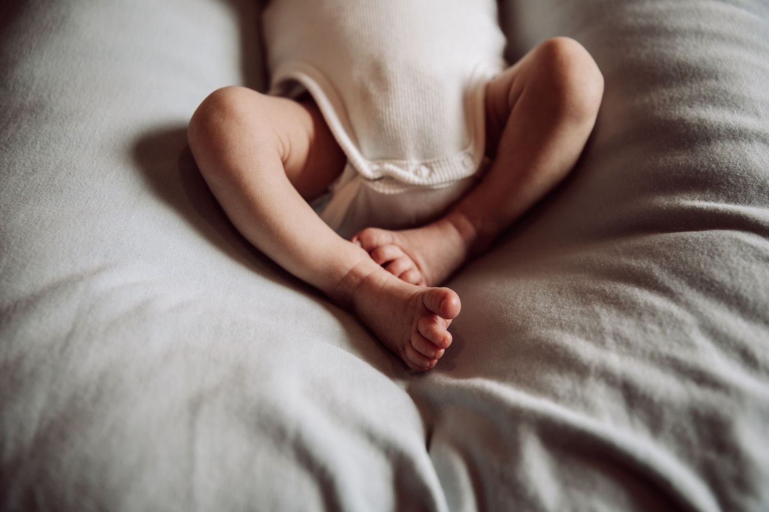 Close-up of tiny newborn baby feet resting on light gray bedding.