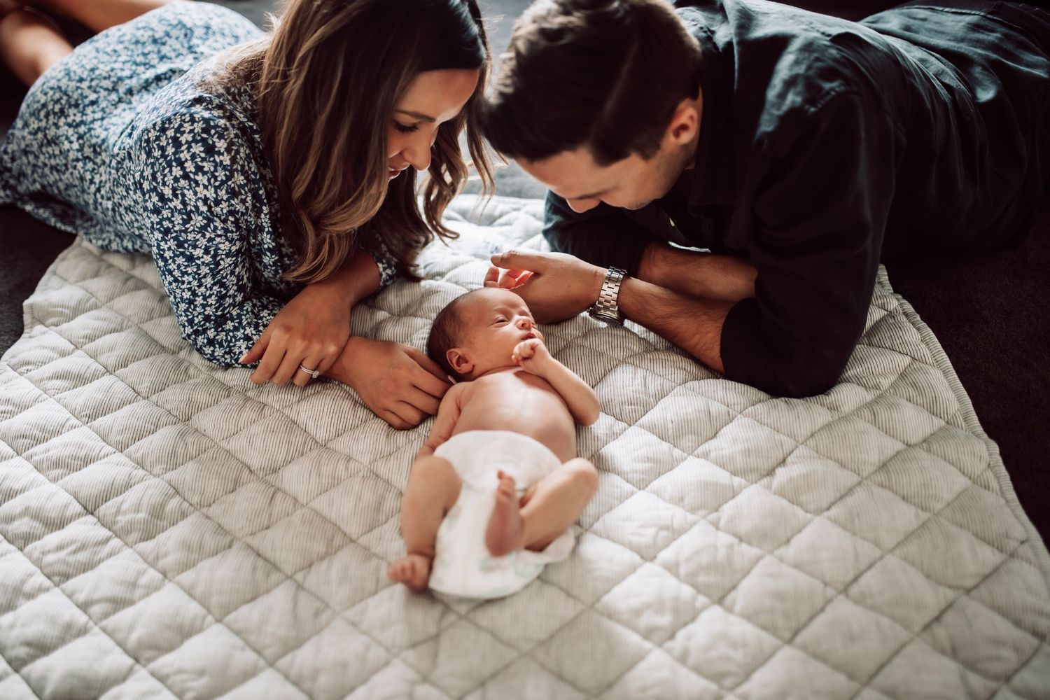 Intimate family photoshoot on a quilted white surface showing tender moments with a newborn.