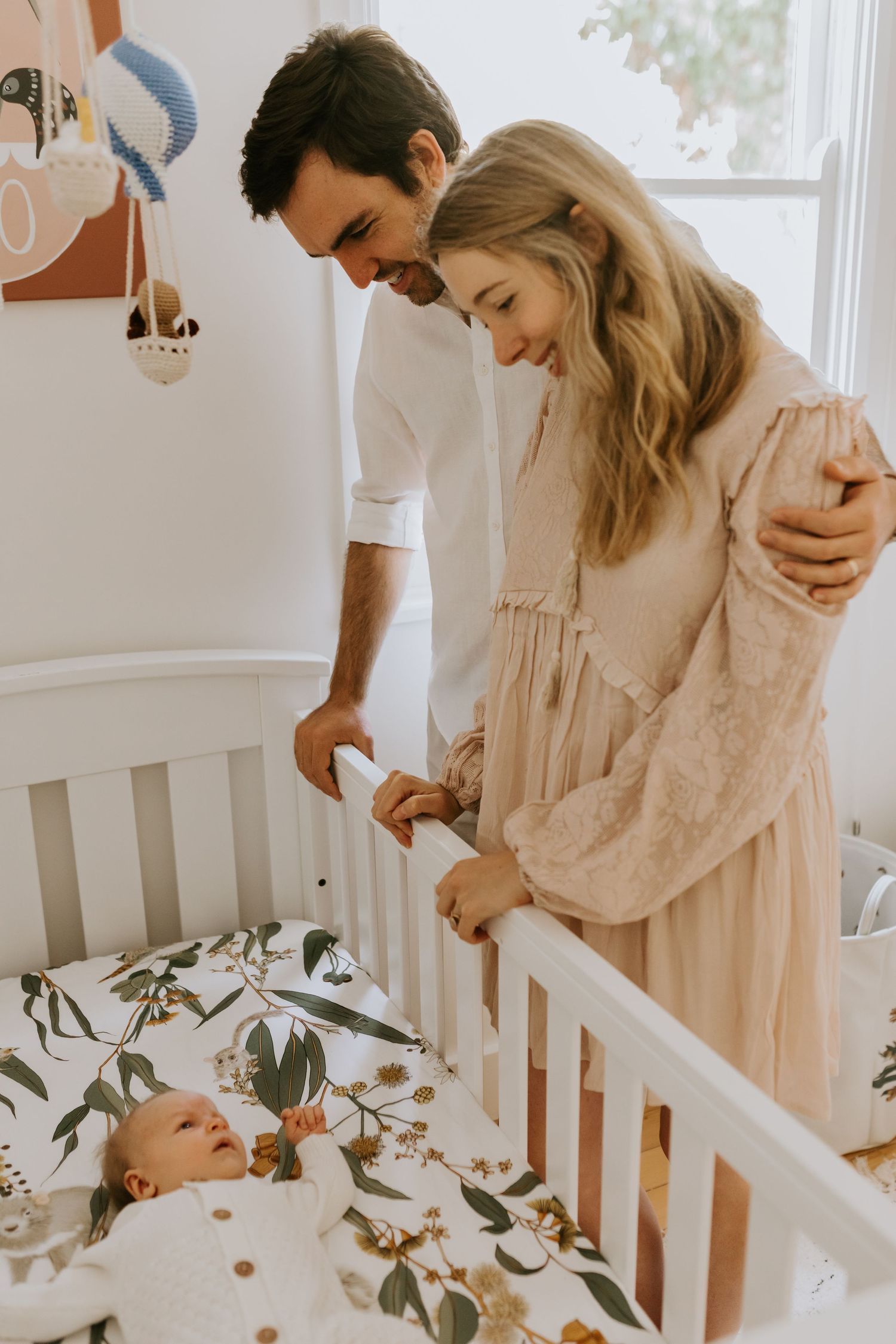 Sweet family moments captured by white crib with botanical garland decoration.