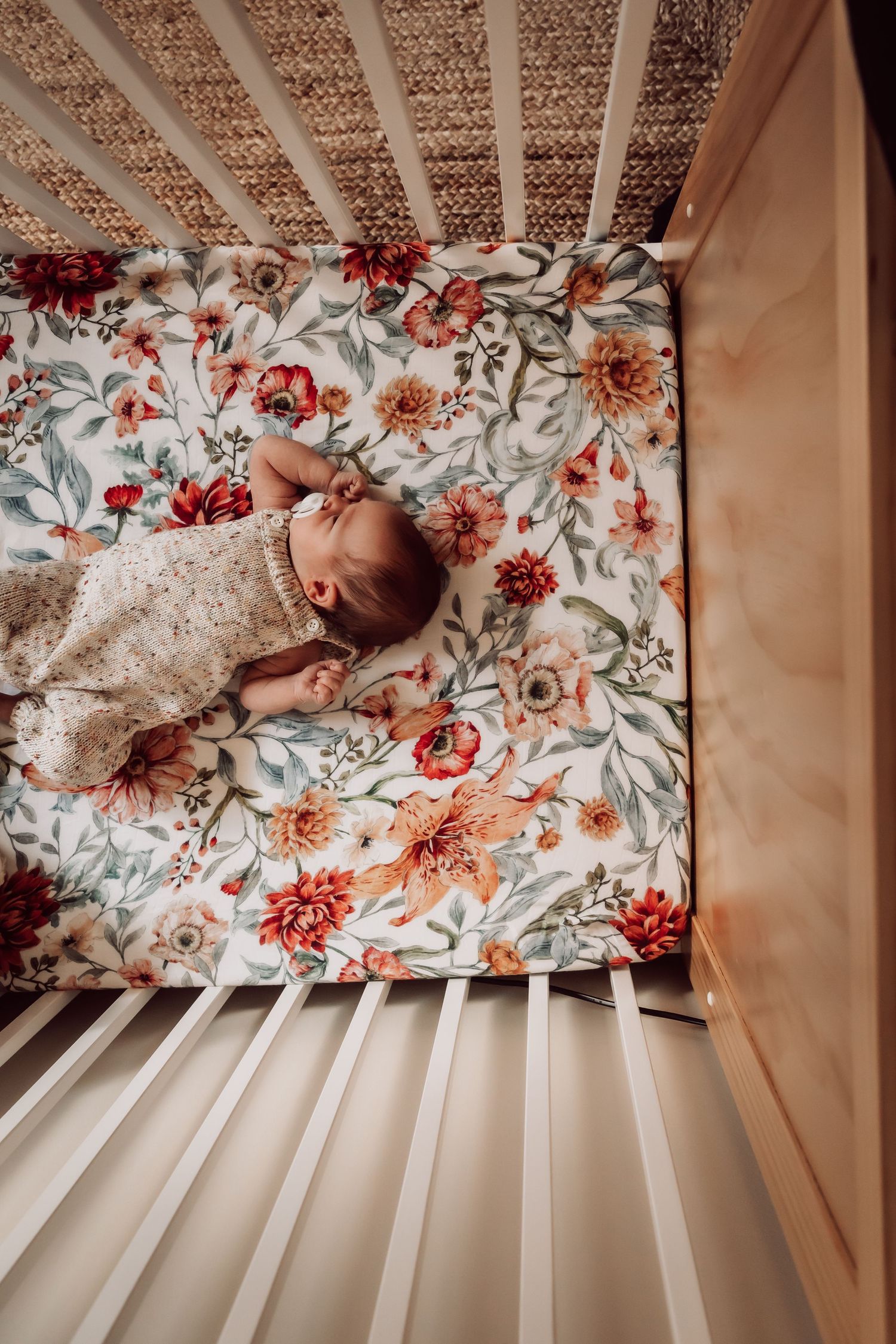 Sleeping baby in floral crib bedding viewed from above.