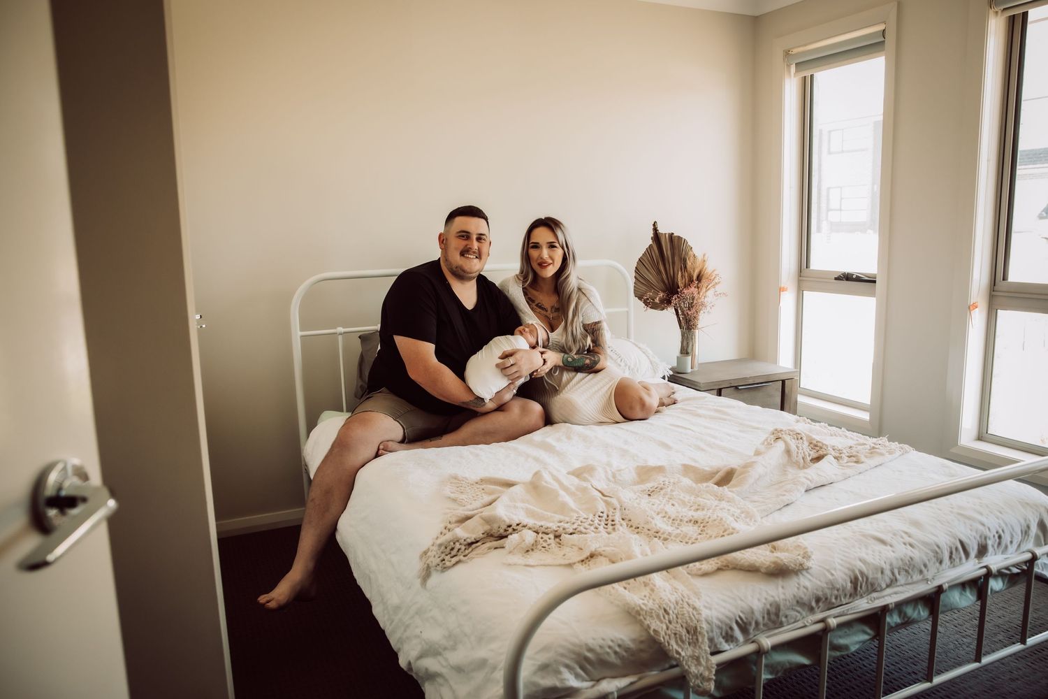 Family sitting together on bed with newborn in bright modern bedroom.