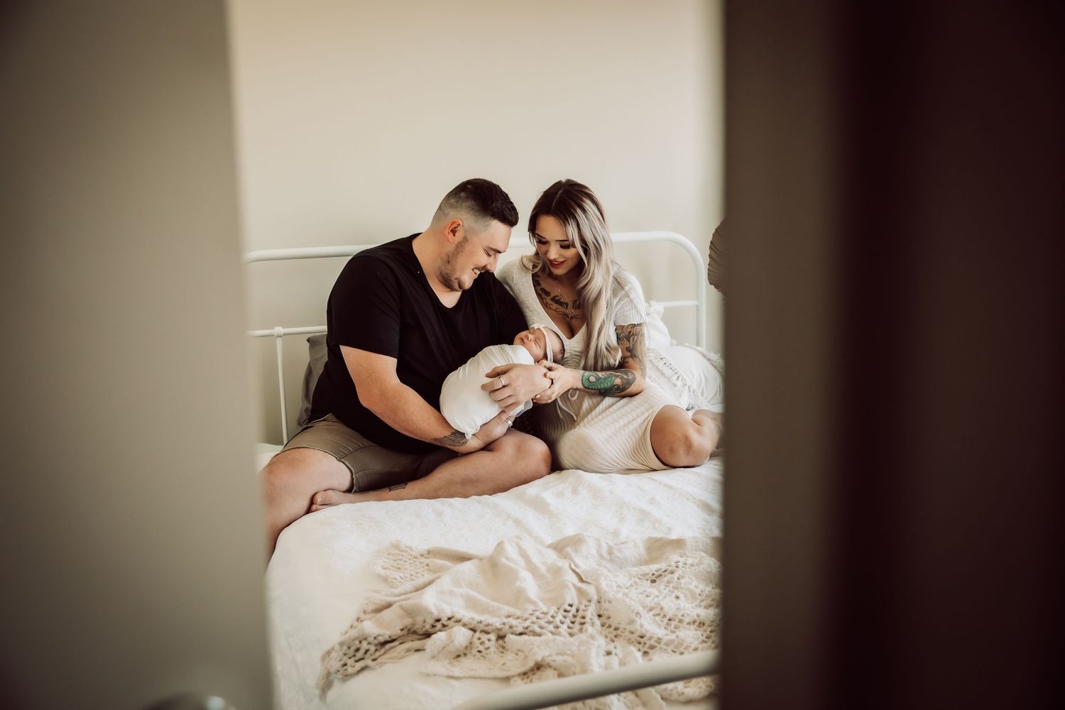 Intimate family moment with newborn baby on bed captured through doorway.