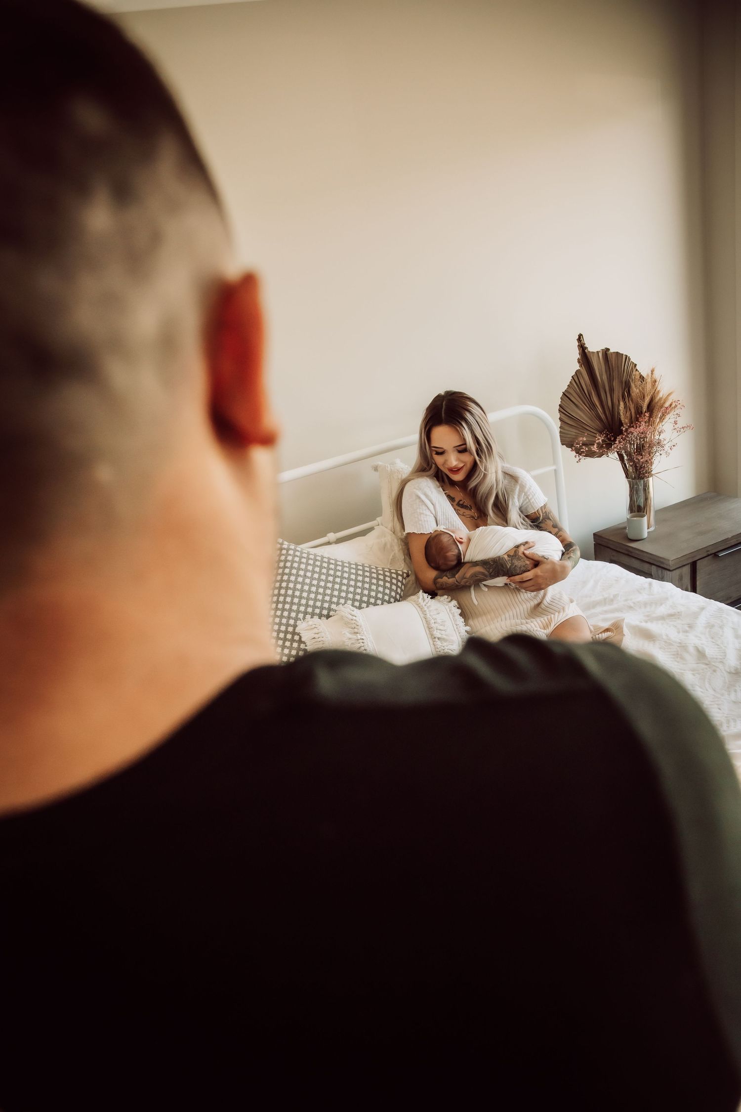 Mother holding newborn baby on bed while being photographed.