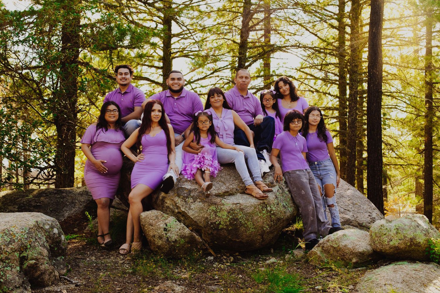 A group wearing matching purple outfits poses together on large rocks in a forest setting.