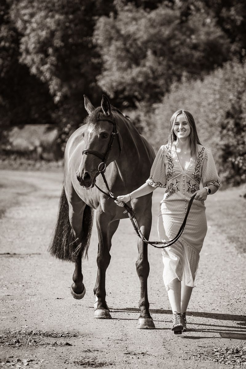 Elegant horse and companion walking together on a tree-lined path in black and white.