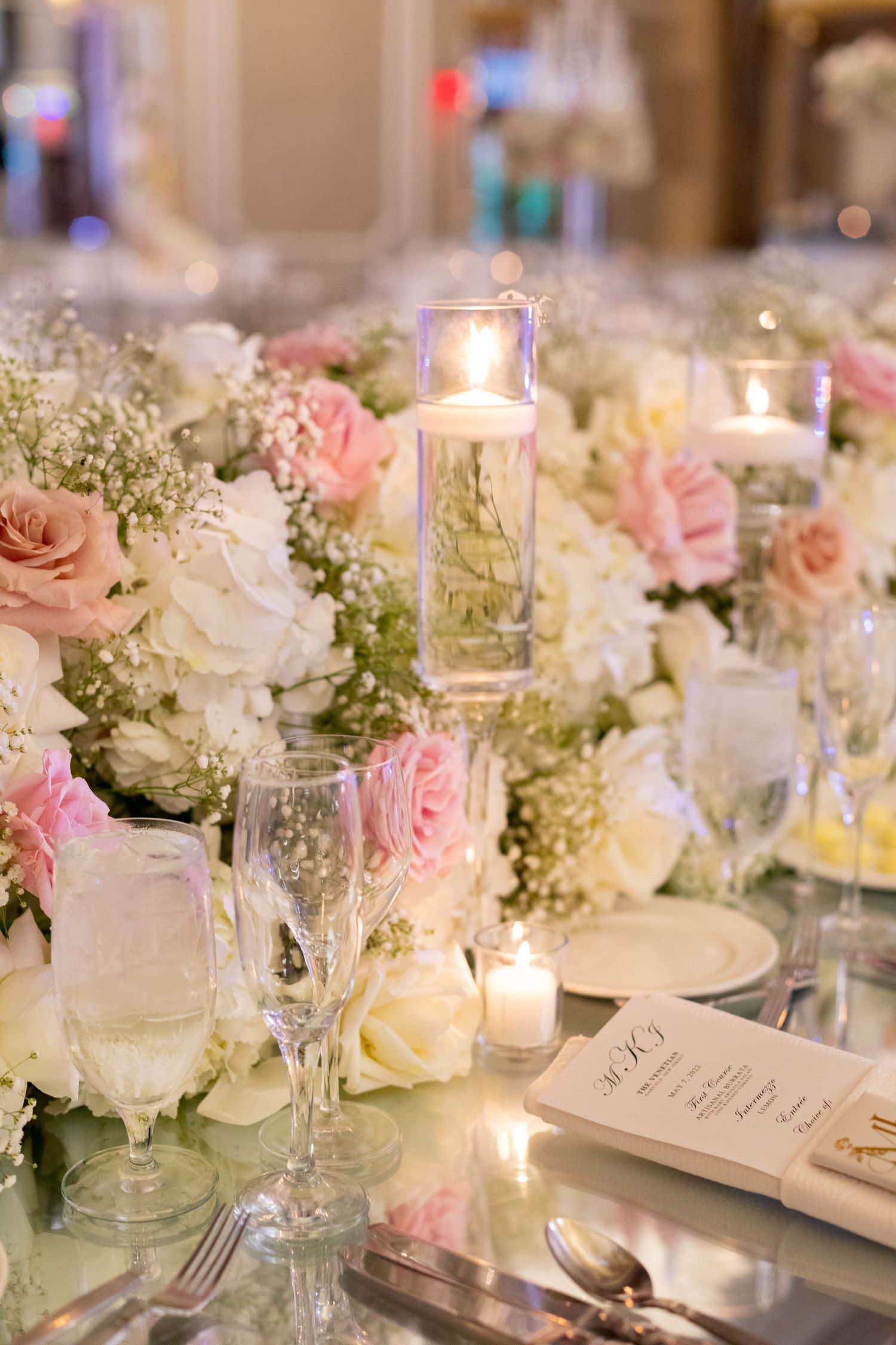 Elegant wedding table setting with pink roses, baby's breath, candles and crystal glassware.