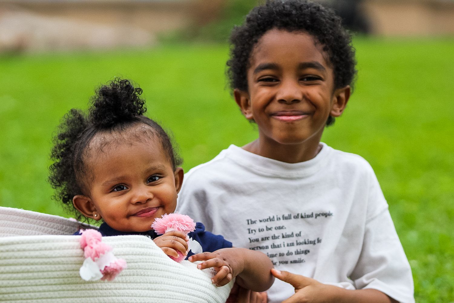 Two siblings share a joyful moment together while sitting outdoors on green grass.