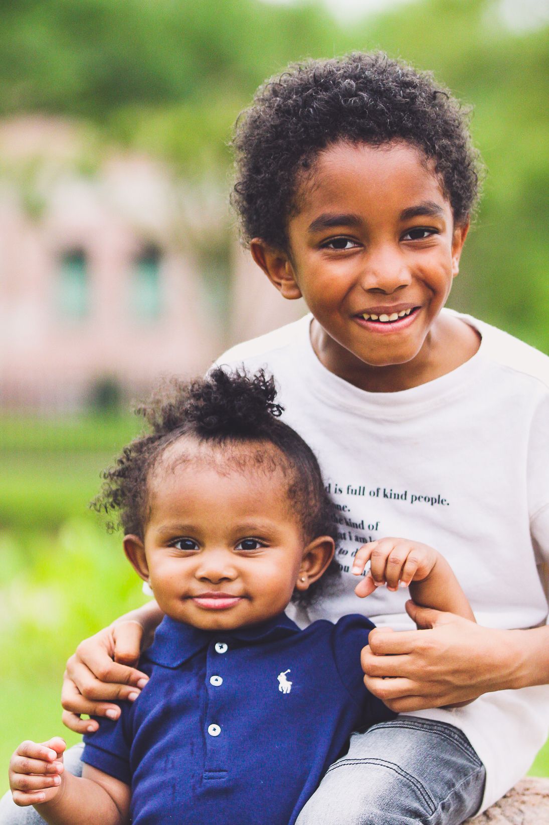 Two siblings share a warm embrace while smiling at the camera outdoors.