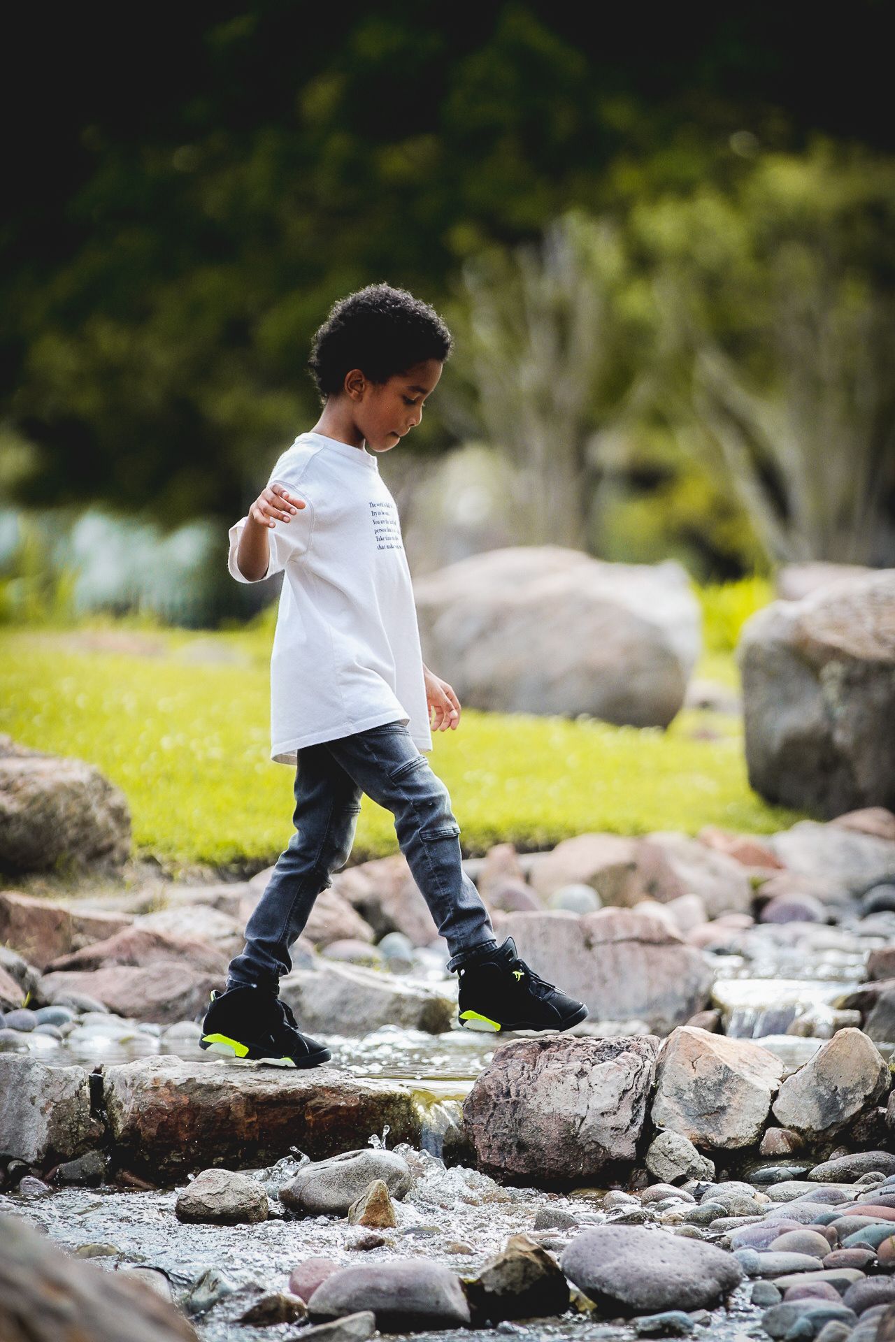 Child in white shirt carefully walks across rocky terrain in a natural outdoor setting.