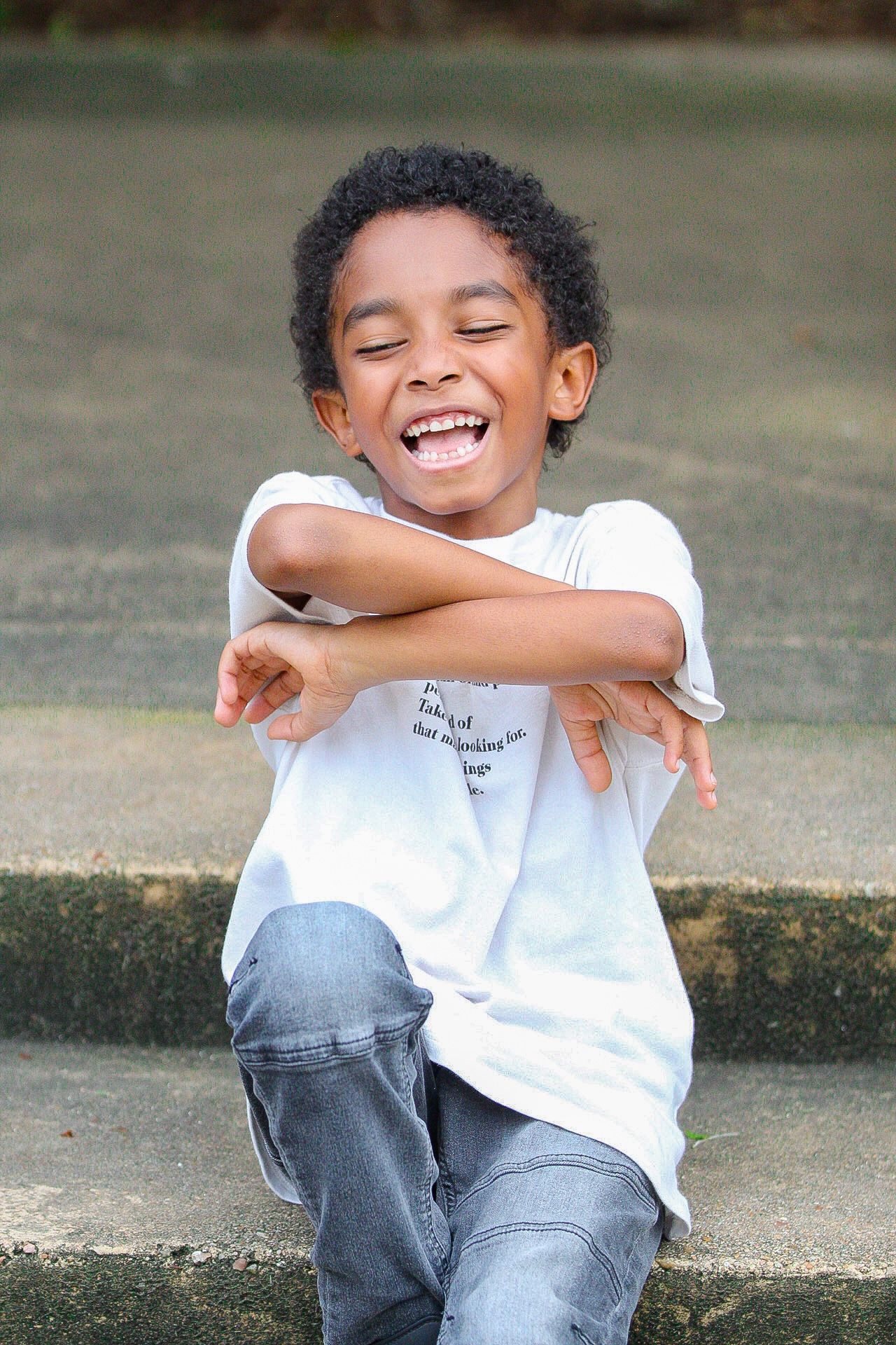 Young child laughing and striking a fun pose while sitting outdoors.