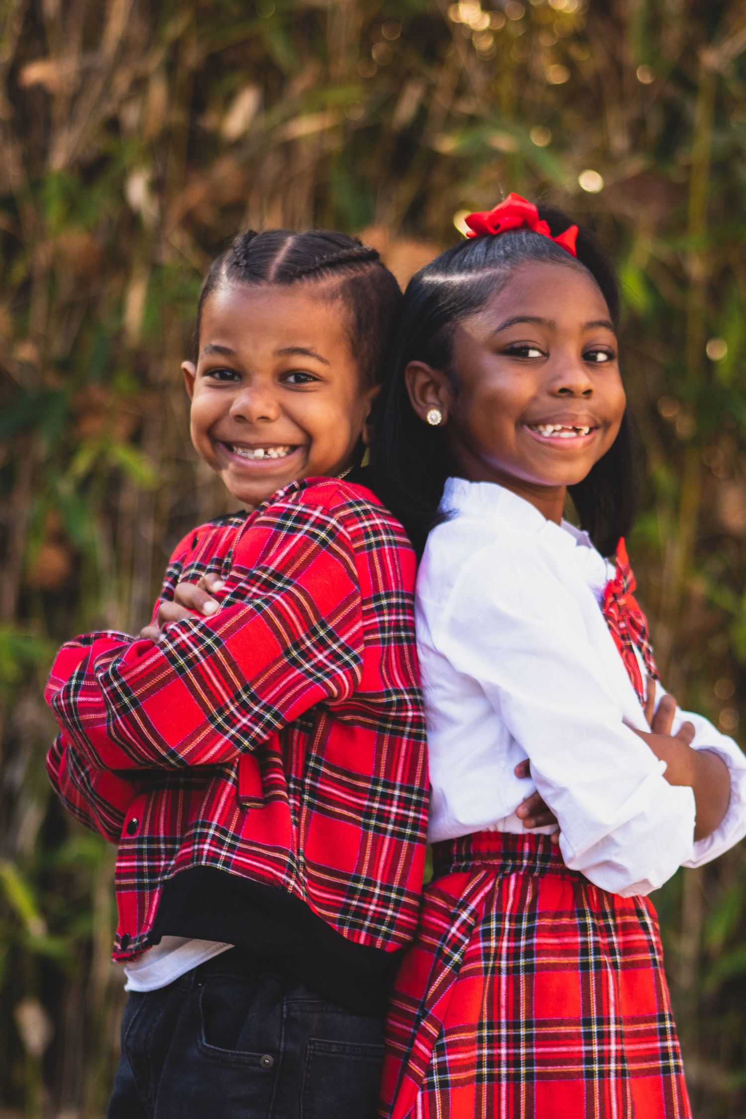 Two children in coordinating red plaid outfits pose back-to-back with bright smiles.