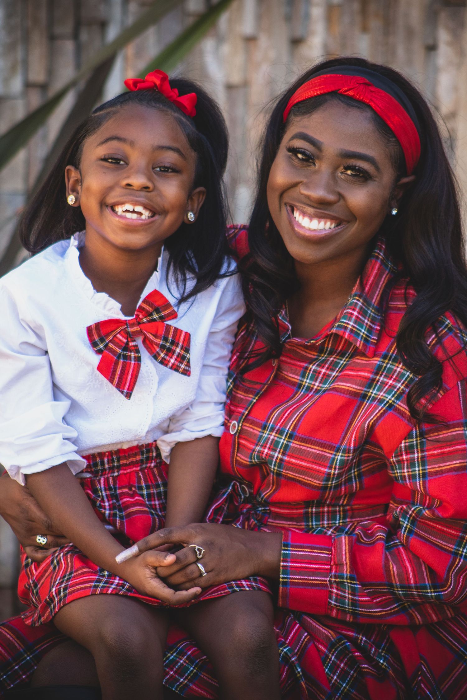Mother and daughter wearing matching red plaid outfits sitting together outdoors.