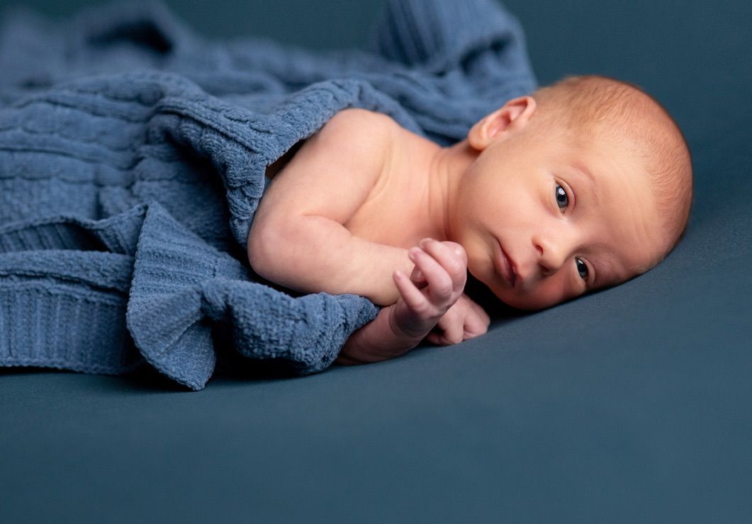 Newborn baby wrapped in blue fabric during professional photo session.