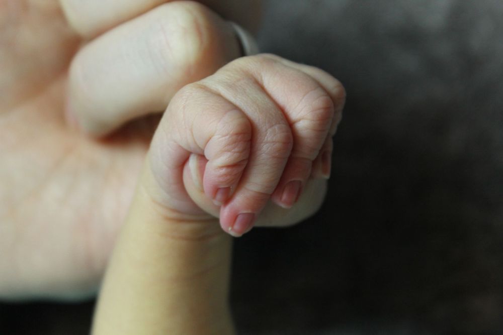 Tiny newborn baby hand gripping an adult's thumb in a close-up photograph.