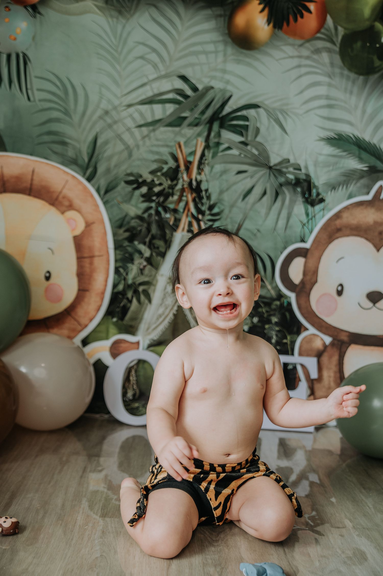 Safari-themed photo session with plush lion and monkey decorations against a tropical leaf backdrop.