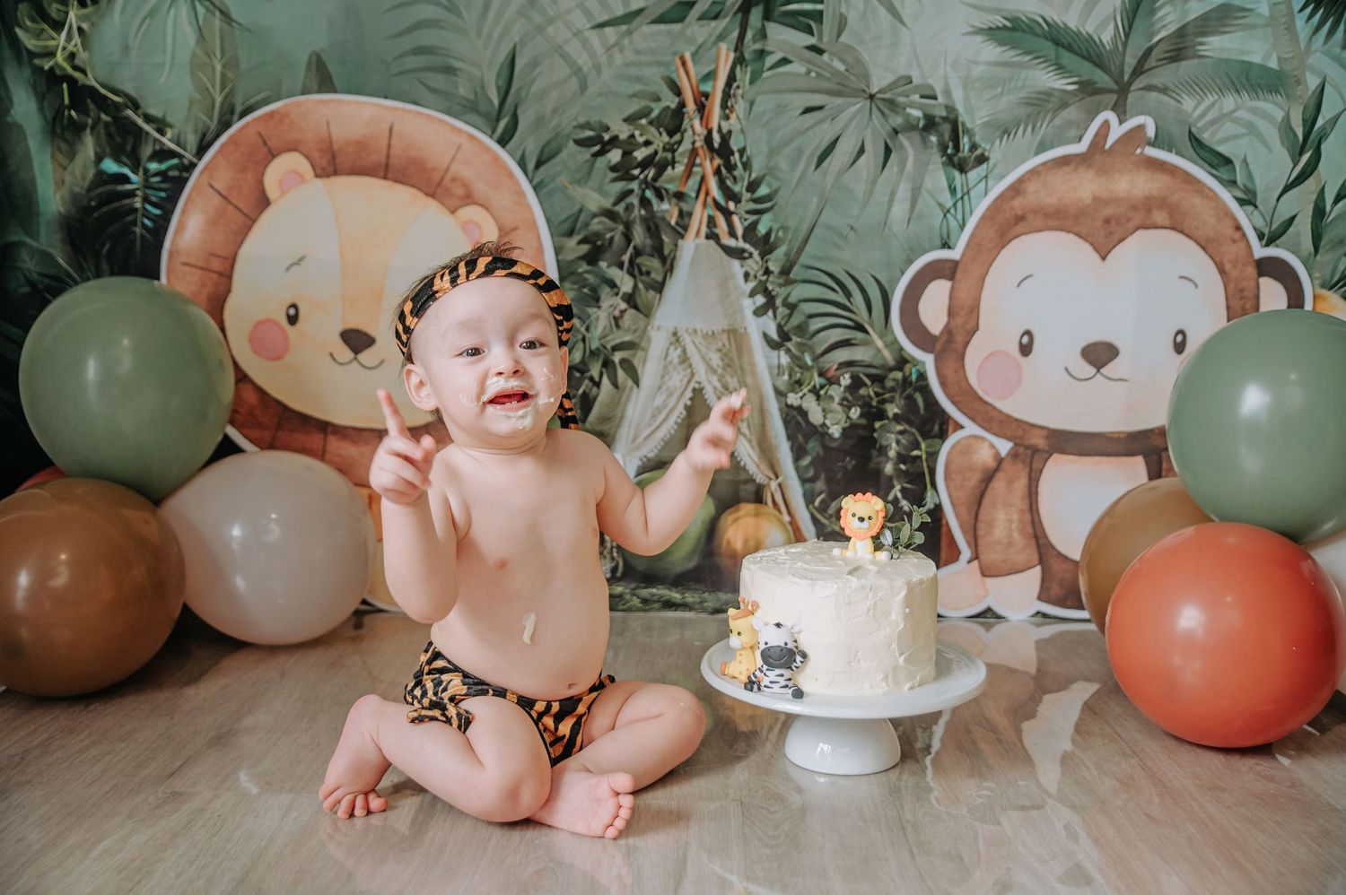 Baby celebrating first birthday with cake and safari themed decorations.