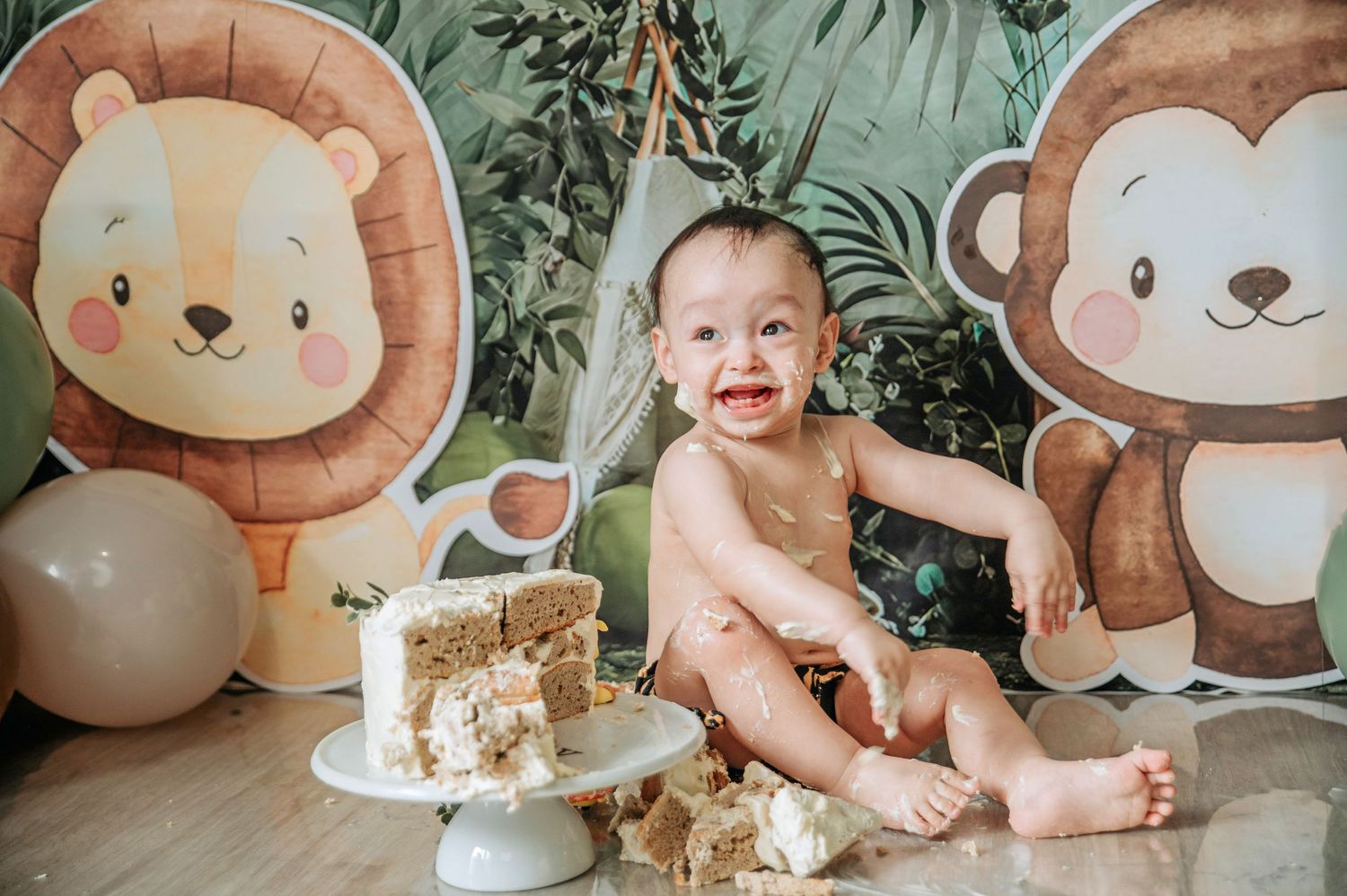 Safari-themed first birthday setup with lion and monkey decorations and a smashed cake on a white stand.