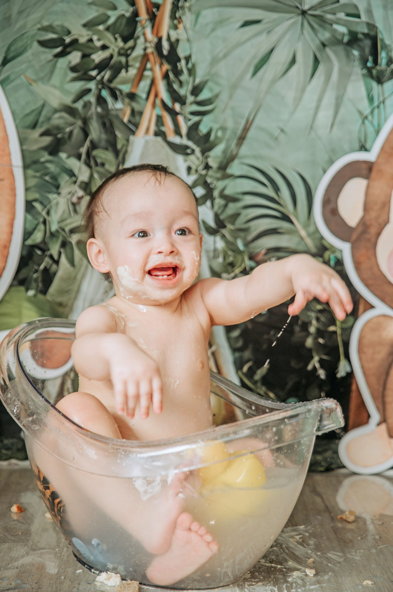 Happy baby splashing in clear bath water with tropical backdrop.