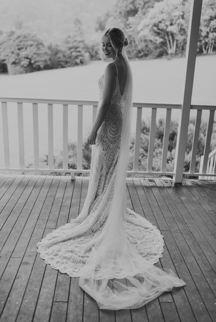 A young bride in her detailed wedding dress, looks down to her shoulder, showing off the low cut back of her gown