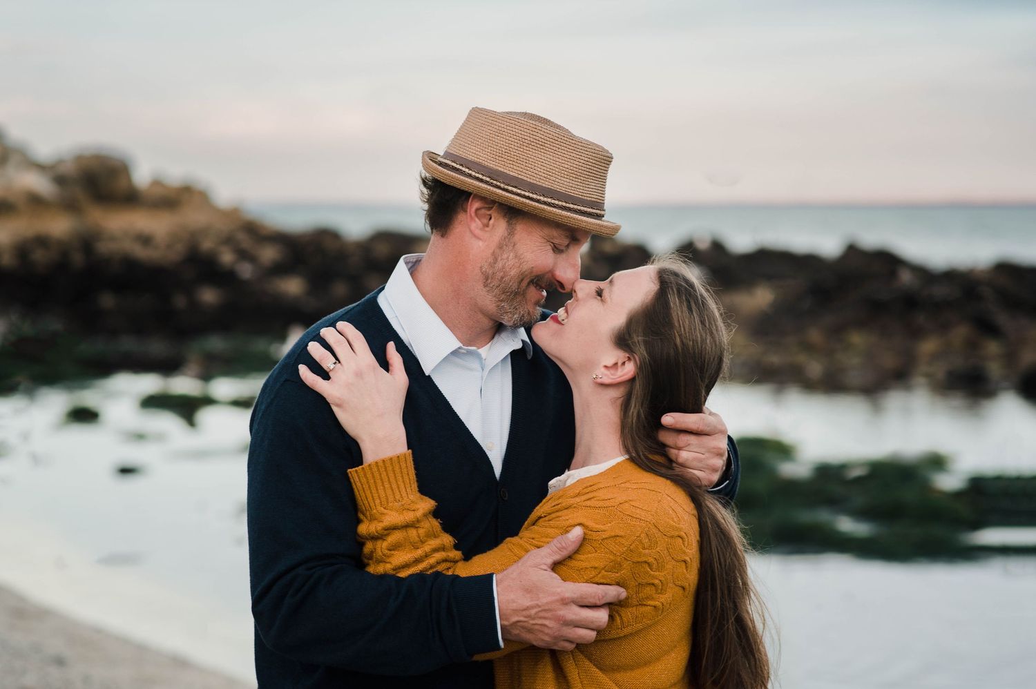 Couple in romantic embrace on rocky beach during sunset.