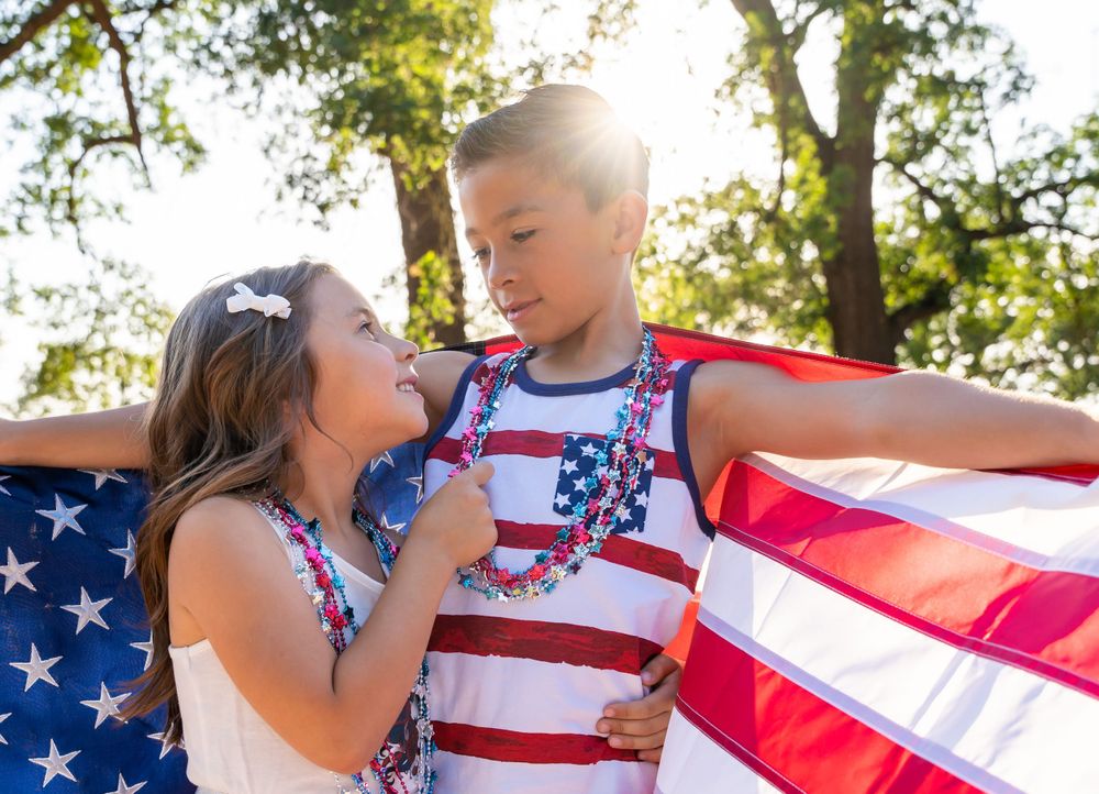 Young brother and sister embracing each other, wrapped in the American flag, celebrating the spirit of patriotism