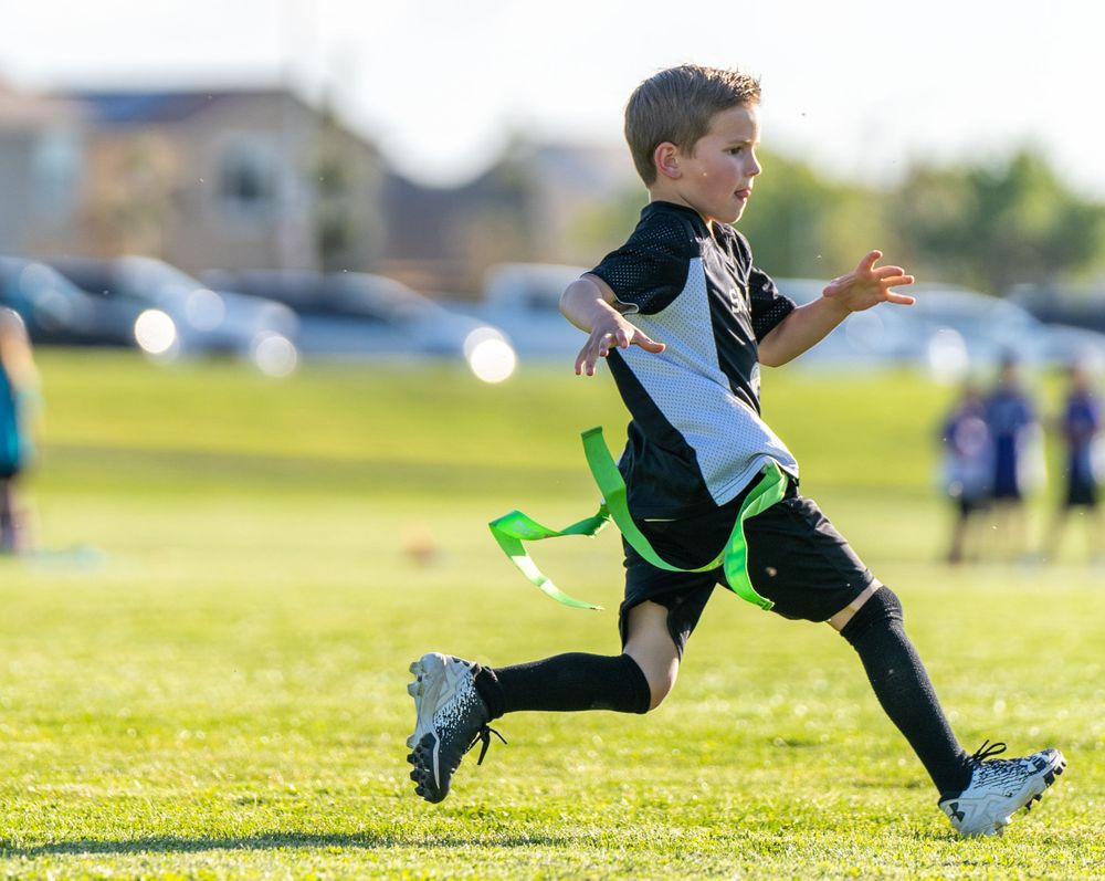 Young boy enthusiastically engaged in flag football game, running with determination and focus