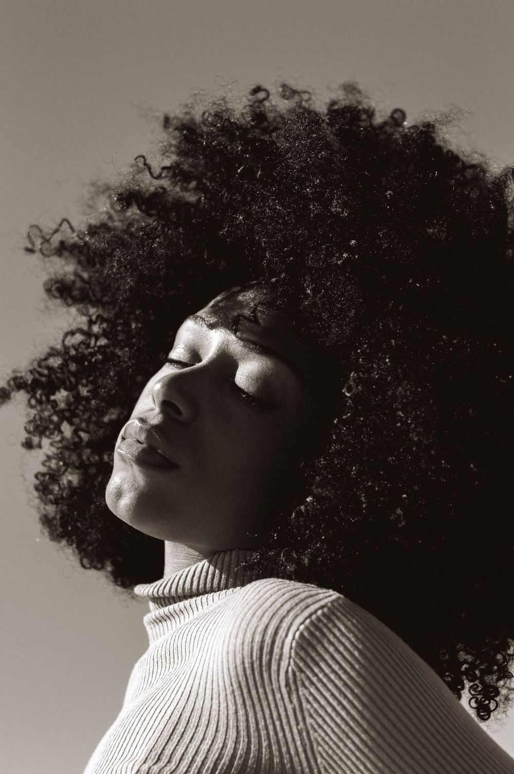 Artistic black and white portrait showcasing natural curly hair and ribbed turtleneck.