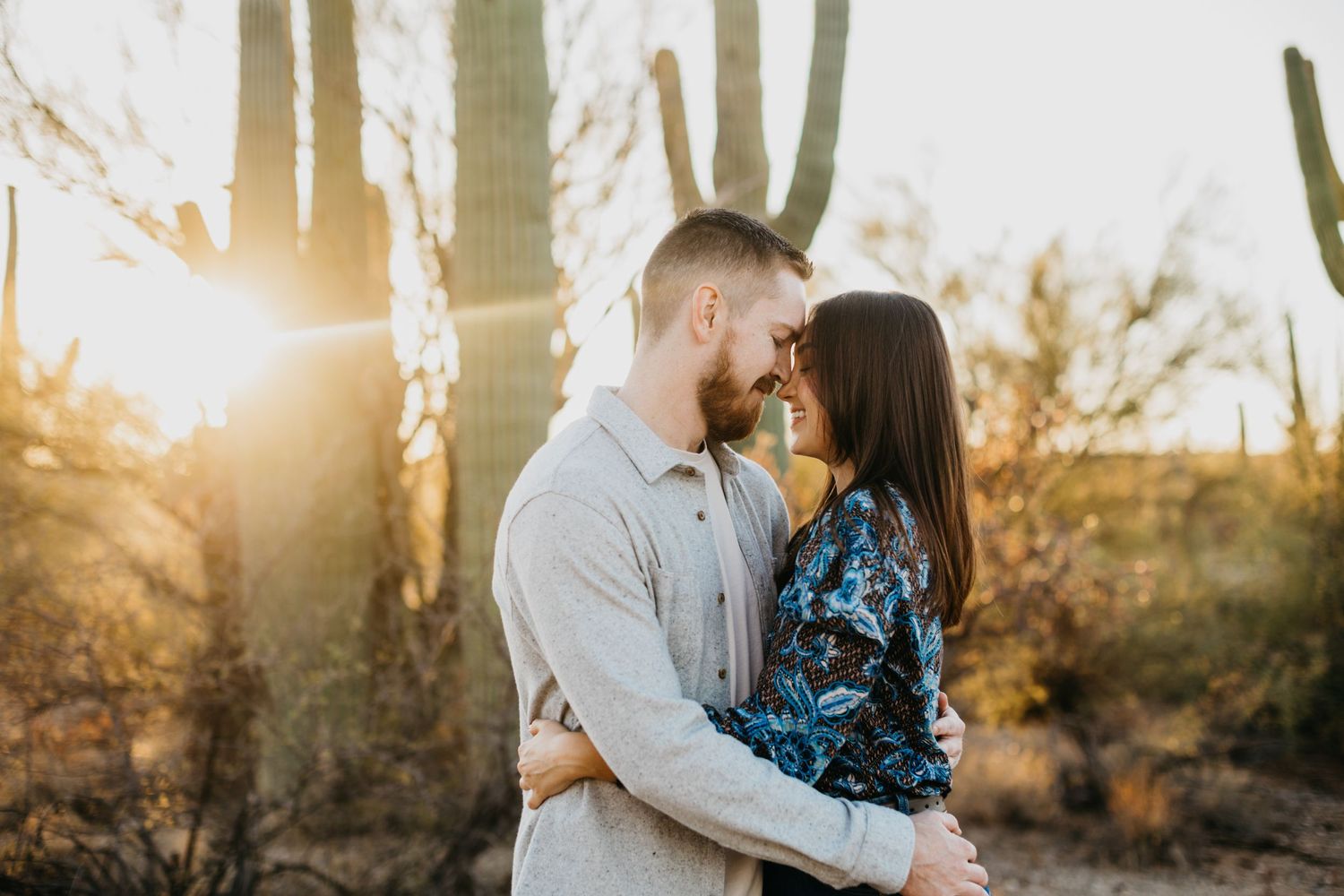 Tucson couples portrait of a man and woman hugging at golden hour with warm sunset light glowing through the trees.