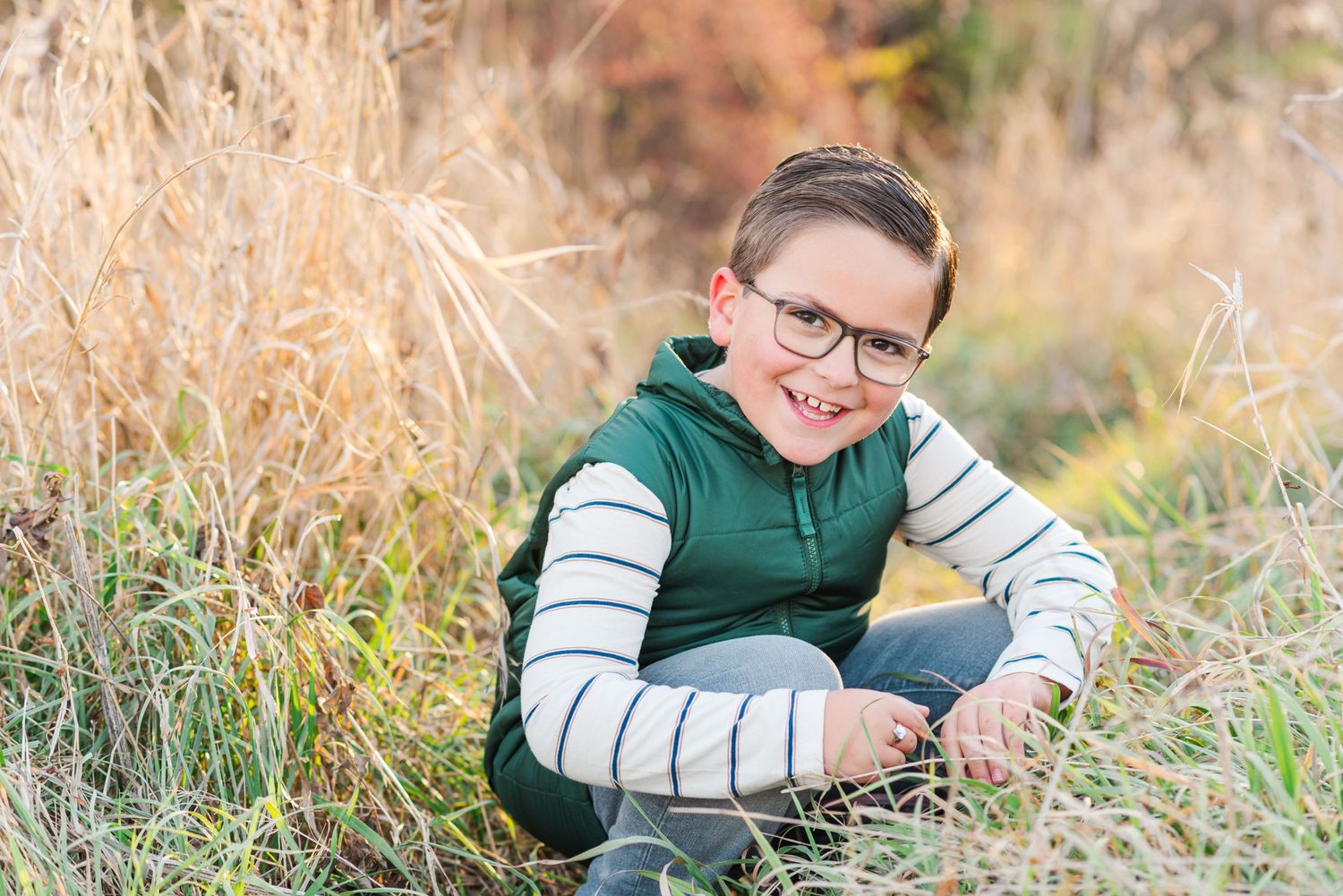 A child sits in tall grass wearing a green and white striped sweater.