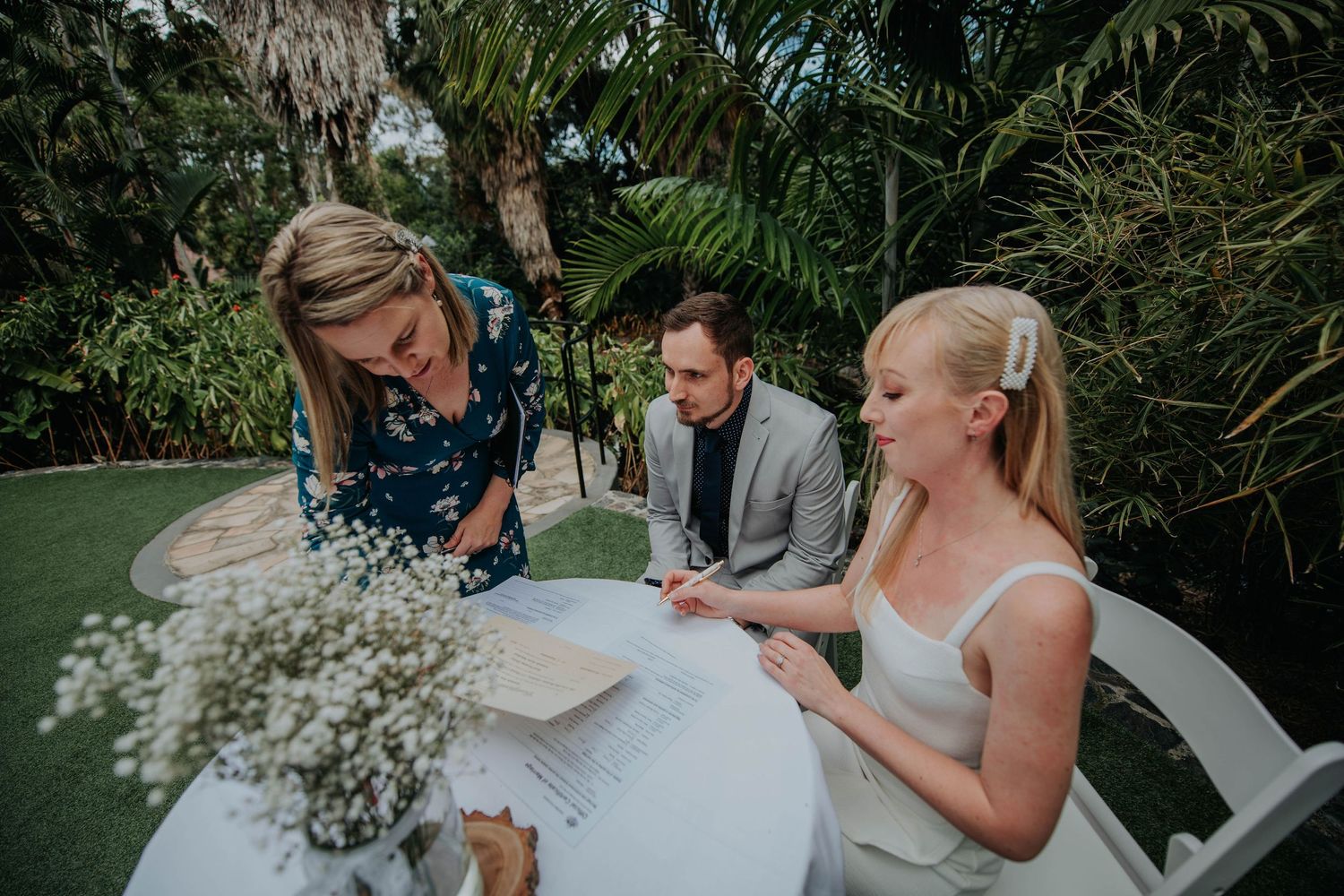 Wedding ceremony paperwork signing in tropical garden setting with witnesses present.