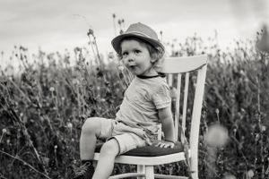Black and white portrait of young child sitting on vintage chair in wildflower field.