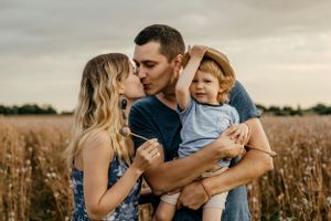 Tender family moment captured in golden wheat field at sunset.